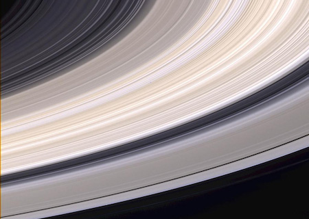 A close up view of Saturn's rings. They are grey and tan, and there are spaces in between where you can see the black color of space through them.