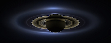 A photo of Saturn where it is backlit by the sun. Saturn and its rings are nearly black, and the sun is making the edges glow.