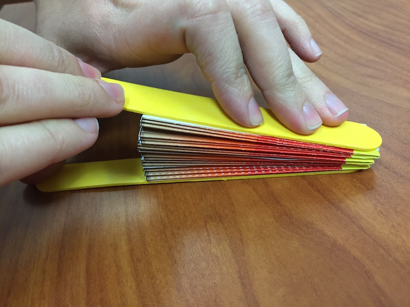 a photo of the second popsicle stick being glued on top of the compressed fan
