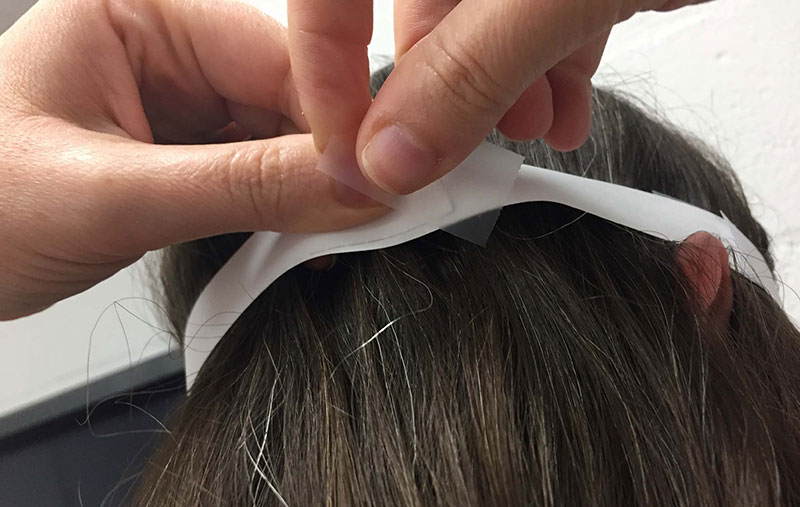 a person wraps a long strip of paper around her head and tapes the paper so that it creates a snug fit