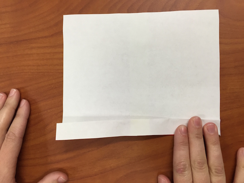 foto del papel dado vuelta de modo que la cara blanca quede hacia arriba, y las manos realizando el segundo pliegue del abanico
