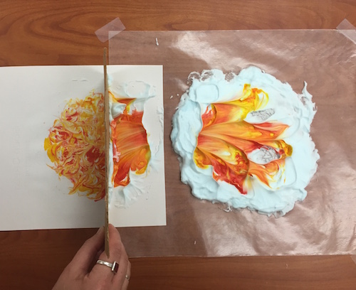 the cardboard squeegee is shown halfway through scraping the shaving creame off the paper