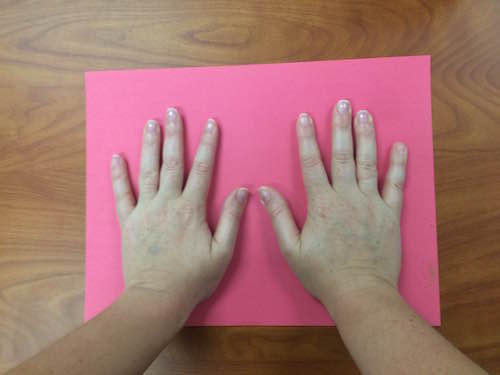 hands placed palm-side-down on a piece of red construction paper