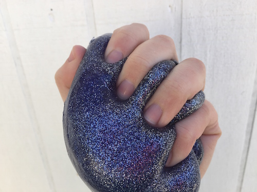 una imagen de una mano sosteniendo un limo morado universo con un montón de brillo